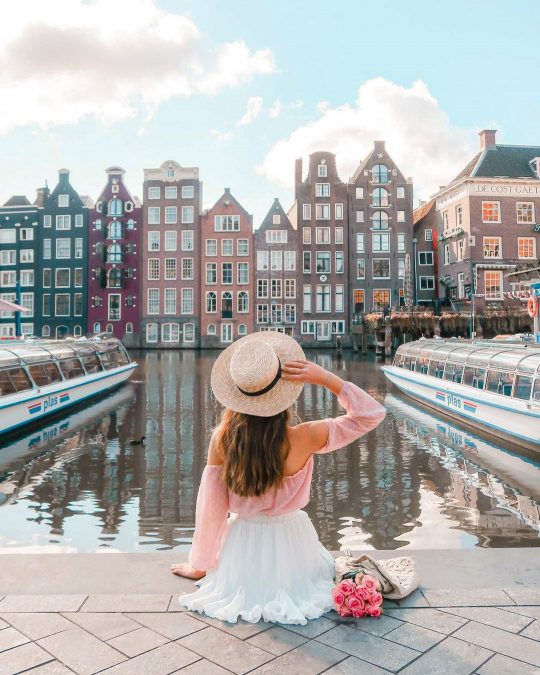 a person admiring the view of Amsterdam's iconic canals and colourful buildings