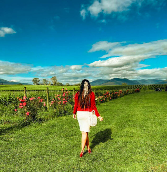 a woman walks through a field of vines in the Yarra Valley, Australia, enjoying the beautiful scenery
