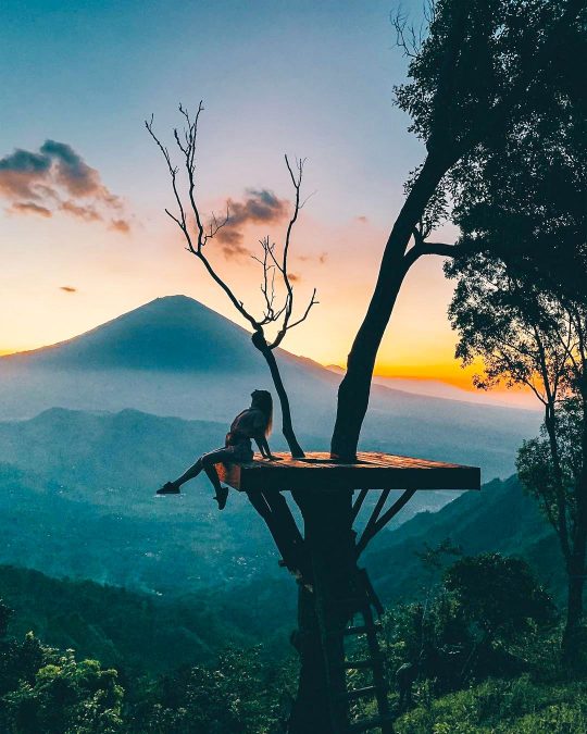 a woman on a tree-top platform watching the mesmerising sunrise behind Mount Agung