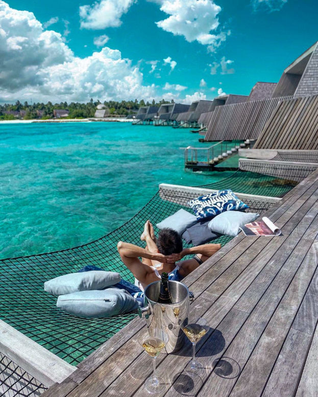 a man in a hammock on a wooden deck overlooking the ocean