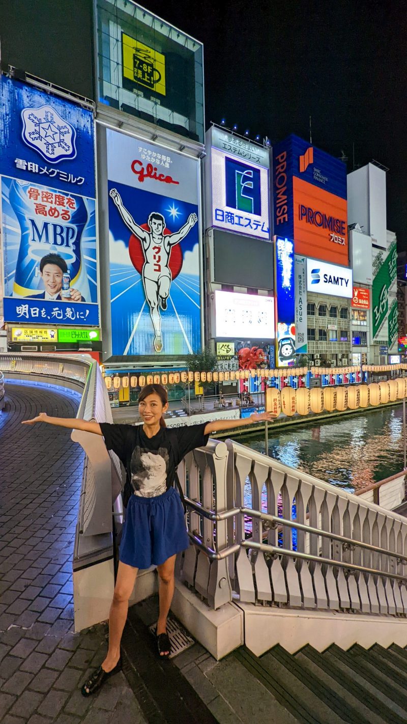 a woman strikes a pose in front of the famous Glico Running Man at Dotonbori, Osaka