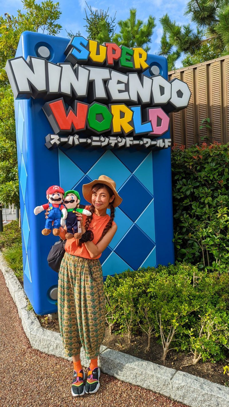 a woman holding Mario and Luigi toys in front of a sign that reads Super Nintendo World