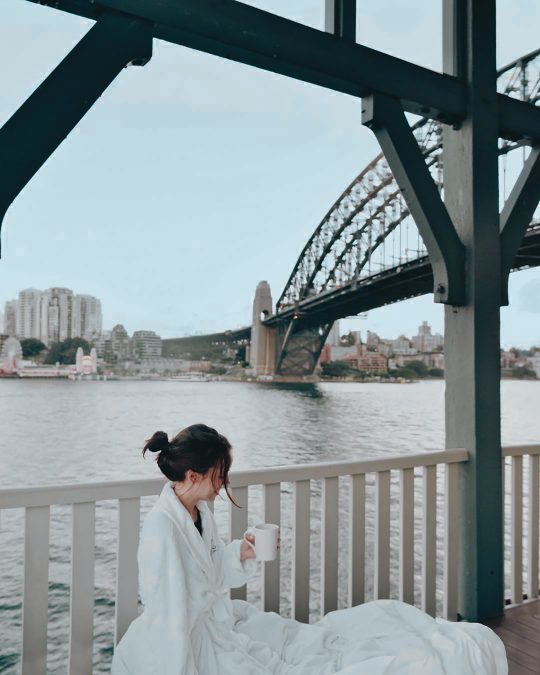 a woman in a white robe enjoying the Sydney Harbour view from the Pier One Sydney Harbour, Autograph Collection