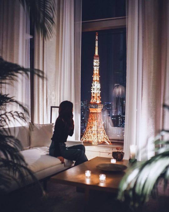 a woman on a couch at The Tokyo EDITION, Toranomon gazes out the window at the TokyoTower