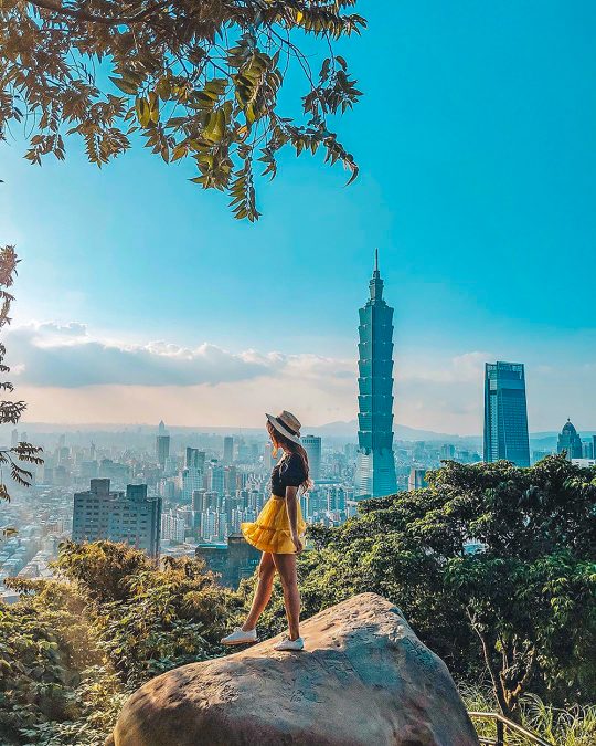a woman standing on a rock overlooking the New Taipei City skyline, Taiwan