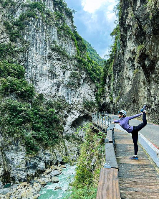 a woman stretching on a wooden bridge over a river in a canyon in Hualien County, Taiwan