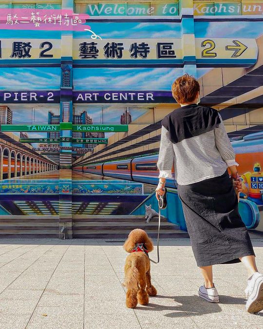 a woman walking a dog in front of a mural of the Kaohsiung cityscape in Pier-2 Art Center, Kaohsiung County, Taiwan