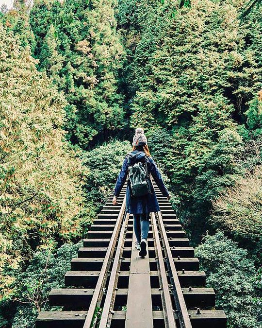 a person walking on the elevated wooden railway tracks of the Alishan Forest Railway in Chiayi County, Taiwan