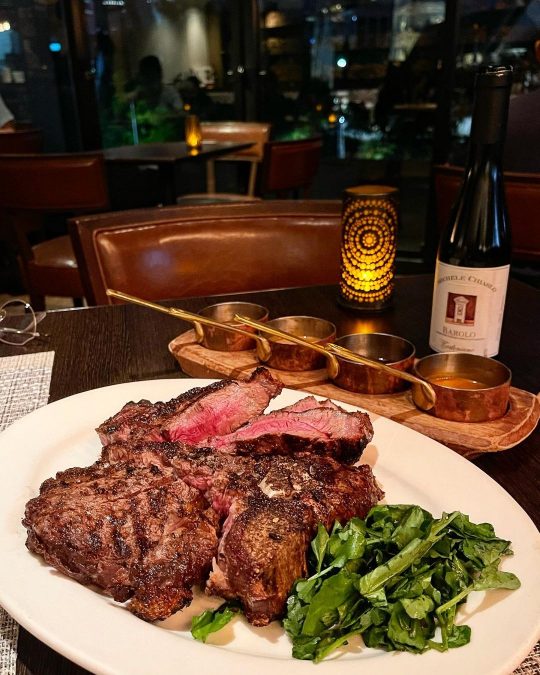 a thick slab of Porterhouse steak with vegetable sides and sauces paired with wine